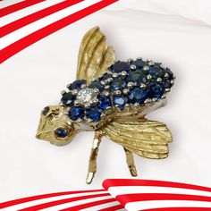 The Blue Sapphire & Diamond Bee Brooch or Pendant is a charming estate piece that features a prong-set diamond and round-cut blue sapphires. The safety clasp pin and hidden bail provide secure wear, while the sapphires surrounding the diamond create a striking body for the bee. Each sapphire is expertly color and clarity matched for a stunning overall appearance. This item is two-tone. Metal: 18 karat yellow & white gold Finish: Polished and Textured Gemstone color: Blue Sapphire, F,G color rang Blue Sapphire Brooches As Gift, Fine Jewelry Blue Brooches For Anniversary, Blue Fine Jewelry Brooches For Anniversary, Blue Sapphire Brooch For Gift, Blue Sapphire Brooches For Gift, Blue Diamond Brooches For Anniversary, Luxury Sapphire Brooches As Gifts, Blue Diamond Gemstone Brooches, Luxury Blue Sapphire Brooch