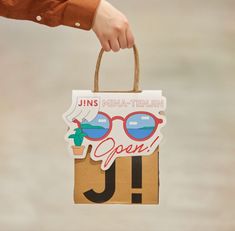 a person holding a paper bag with sunglasses on it and the words j is for miniatrium open