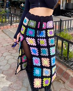 a woman wearing a black crop top and colorful crochet skirt with thigh high boots