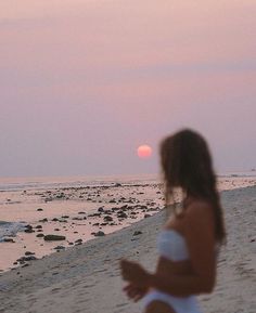 a woman walking on the beach at sunset