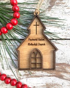 a wooden ornament with a church on it next to some red berries and pine needles