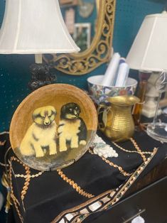 two cats sitting in a bowl on top of a table next to a lamp and mirror