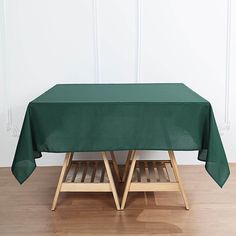 a green table cloth on top of two wooden chairs in front of a white wall