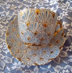 two cups and saucers sitting on top of a blue table cloth with white lace