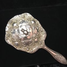 a silver spoon with ornate designs on it sitting on a black velvet surface next to a metal object