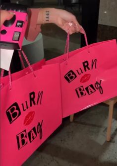 two pink bags with the words burn, bank and lipstick on them are being held by a woman's hand