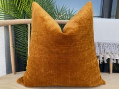 a brown pillow sitting on top of a wooden chair next to a plant and window