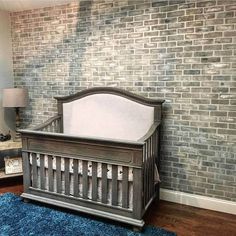 a baby crib in front of a brick wall with a blue rug on the floor