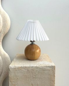 a table lamp sitting on top of a block of cement next to a white vase