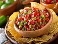 a wooden bowl filled with salsa surrounded by tortilla chips