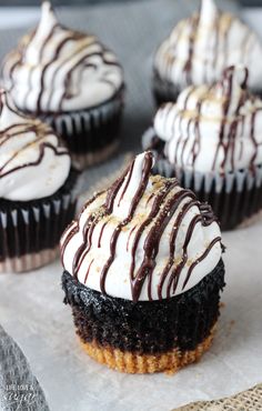 chocolate cupcakes with white frosting and drizzled on top sitting on a piece of parchment paper