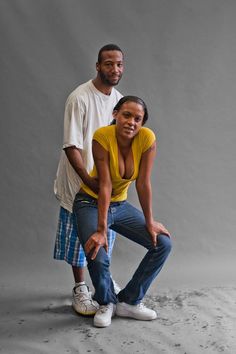 a man and woman posing for a photo in front of a gray background with sand on the ground