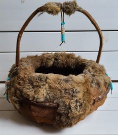 a basket with fur and beads hanging from it's side on a white surface