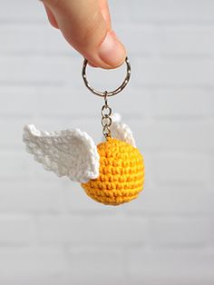 a hand holding a crocheted keychain with an angel wing on it