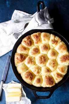 a cast iron skillet filled with bread and cheese on a blue surface next to butter