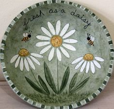 a green bowl with white daisies and bees painted on the side that says fresh as a daisy