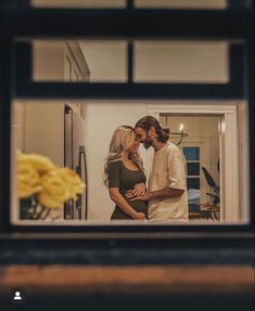 a man and woman standing next to each other in front of a kitchen window looking at each other