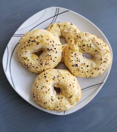 four bagels on a white plate with black sprinkles sitting on a table