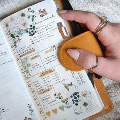 a person is holding a small wallet in front of an open planner with flowers on it