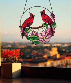 a stained glass window with two birds hanging from it's sides and flowers in the foreground