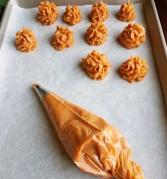 some cookies are on a baking sheet with a cookie scoop in the foreground and an orange candy