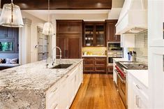 a large kitchen with wooden floors and white cabinetry, along with marble counter tops