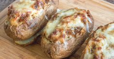 three baked potatoes sitting on top of a wooden cutting board with cheese and meat toppings