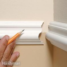 a hand is holding a pencil and pointing at the corner of a wall with molding on it