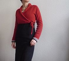 a woman standing in front of a white wall wearing a red sweater and black skirt