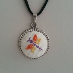 a cross stitch necklace with an orange and purple flower on it