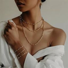 a woman wearing a white shirt and gold necklace with multiple chains on her chest,