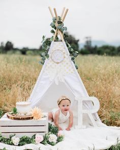 a baby is sitting in front of a teepee with flowers and greenery on it