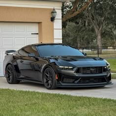 a black sports car parked in front of a house with a garage door on the side