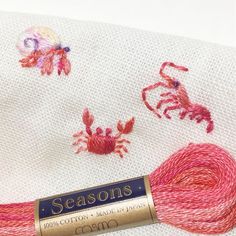 a close up of a needle and thread on a white cloth with crab embroidery designs