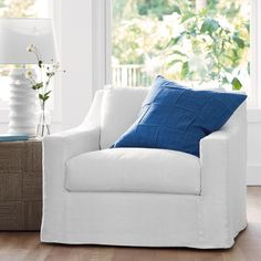 a white chair sitting in front of a window next to a basket filled with flowers