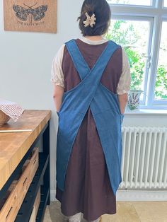 a woman standing in front of a window with a blue apron on her back,