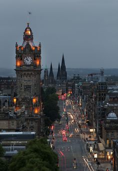 a city street at night with cars driving on it and a clock tower in the background