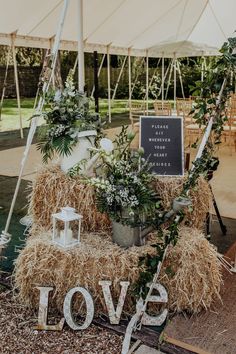 a hay bale with flowers and greenery on the table in front of a large white tent