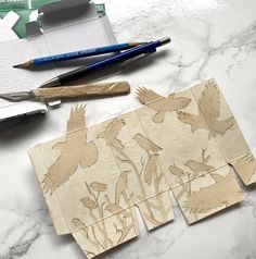 several pieces of wood cut out to look like birds on a marble table with markers and pencils