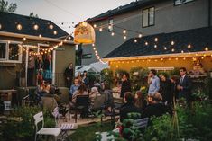 a group of people are gathered outside in the yard for an outdoor party with string lights