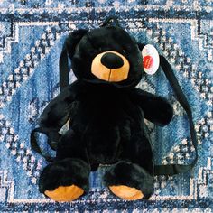 a black teddy bear sitting on top of a blue rug next to a small bag