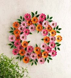 a wreath made out of paper flowers on a wall next to a potted plant