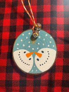 a wooden ornament with two birds painted on it's face, sitting on a red and black checkered table cloth