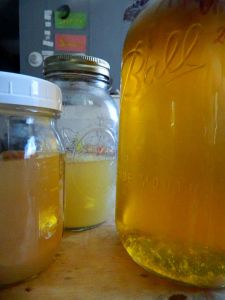 two jars filled with yellow liquid sitting on top of a wooden table next to each other