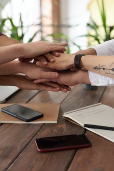 several people holding hands over a wooden table with notebooks and cell phones on it