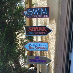 several signs on the side of a building that say swim, shark rising, do not feed the sharks and no swimming