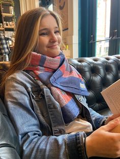 a woman sitting on a couch holding a book in her hands and smiling at the camera