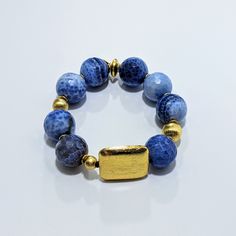 Discover the stunning beauty and unique properties of Ro & Gieo's Blue Fire Agate and 24 Karat Goldplated Brushed Brass Bracelet. Luxurious and eye-catching, this bracelet combines the natural healing energy of blue fire agate with the elegance of 24 karat goldplated brass. Elevate your style and energy with this one-of-a-kind piece. Ro & Gieo Blue Fire Agate & 24 Karat Goldplated Brass Bracelet Bead size - 19 mm 7 inches bracelet length If you want your bracelets in a different size than 7 inch Adjustable Faceted Agate Jewelry, Handmade Blue Agate Bracelets, Agate Healing Bracelet Jewelry, Gold Bracelets With Lapis Lazuli And Natural Stones, Adjustable Sapphire Jewelry With Natural Stones, Spiritual Sapphire Bracelet Jewelry, Gold Lapis Lazuli Bracelet With Gemstone, Gold Lapis Lazuli Gemstone Bracelet, Blue Natural Stone Bangle Jewelry