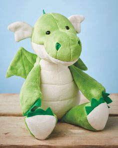 a green stuffed dragon sitting on top of a wooden table