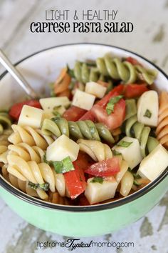 a pasta salad in a green bowl with a spoon and title above it that reads light & healthy caprese pasta salad